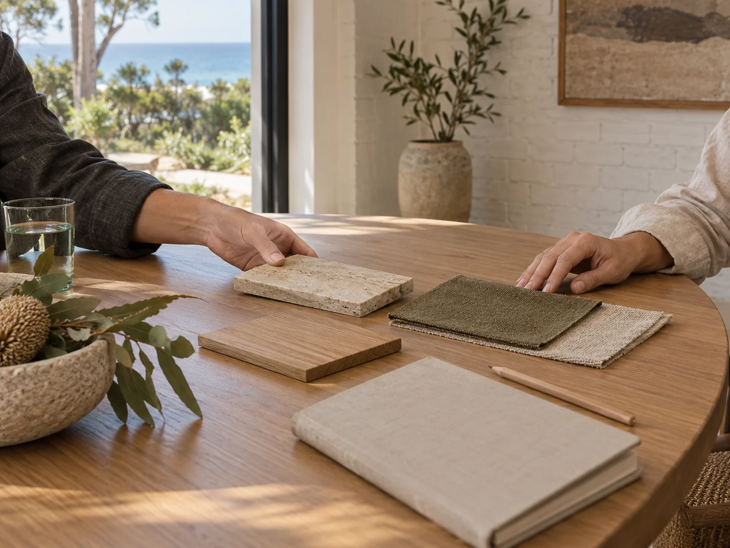 Two people at an oak table moving travertine, oak and linen samples between them during a design consultation
