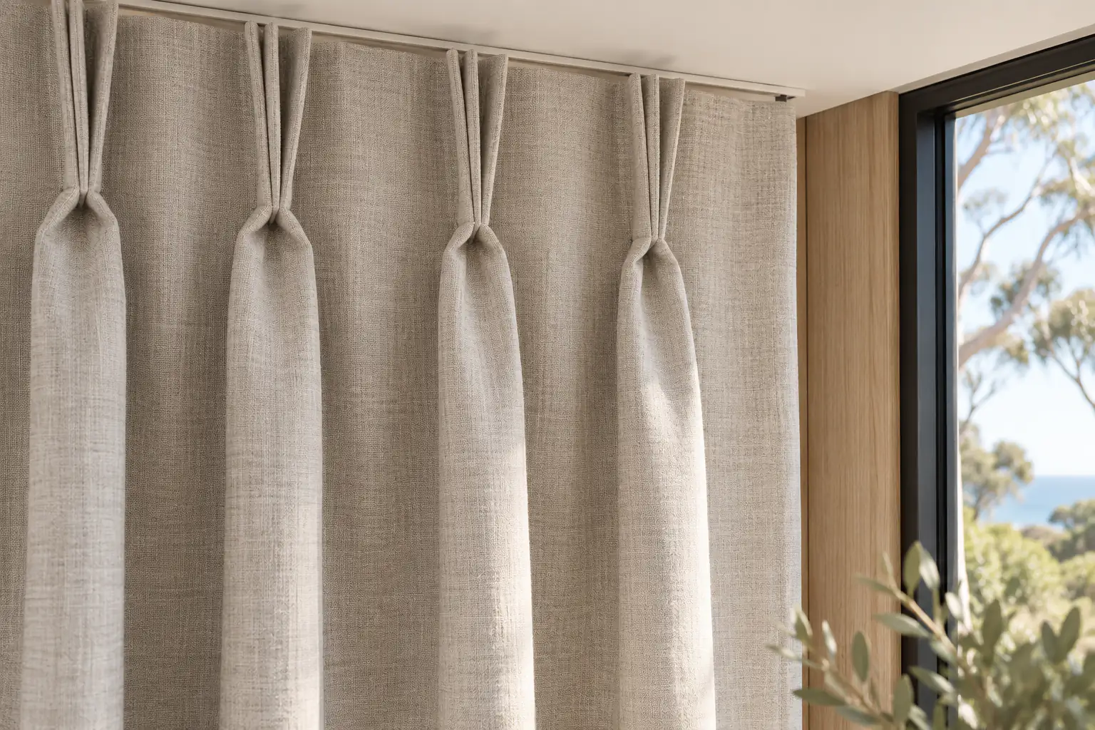 Stitched pinch-pleat groups in oatmeal fabric beside pale timber panelling and a black window frame.