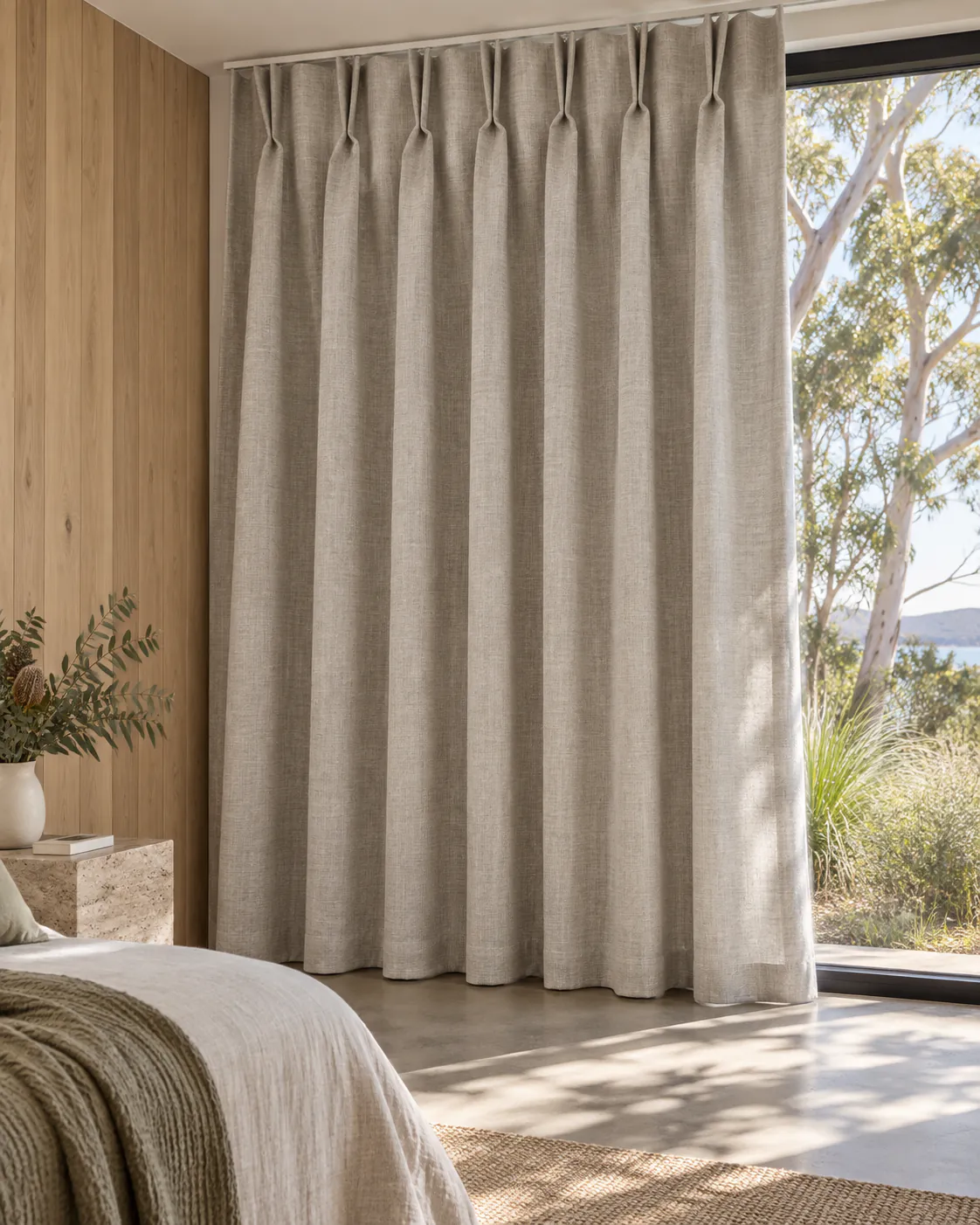 Floor-length pinch-pleat curtains in a timber-panelled room with native greenery outside.