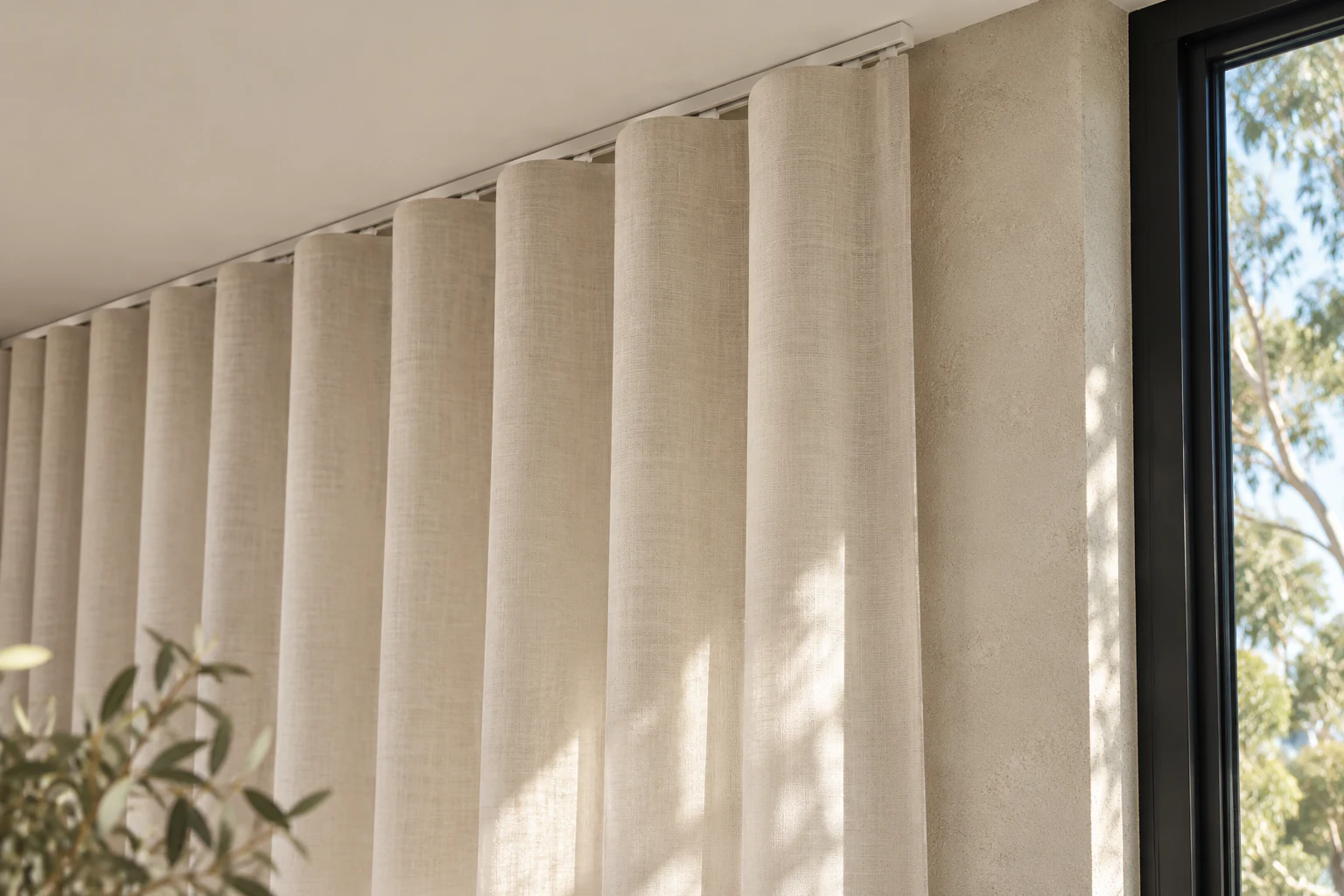 Continuous S-wave heading suspended below a slim curtain track, beside a bagged-render wall and window.