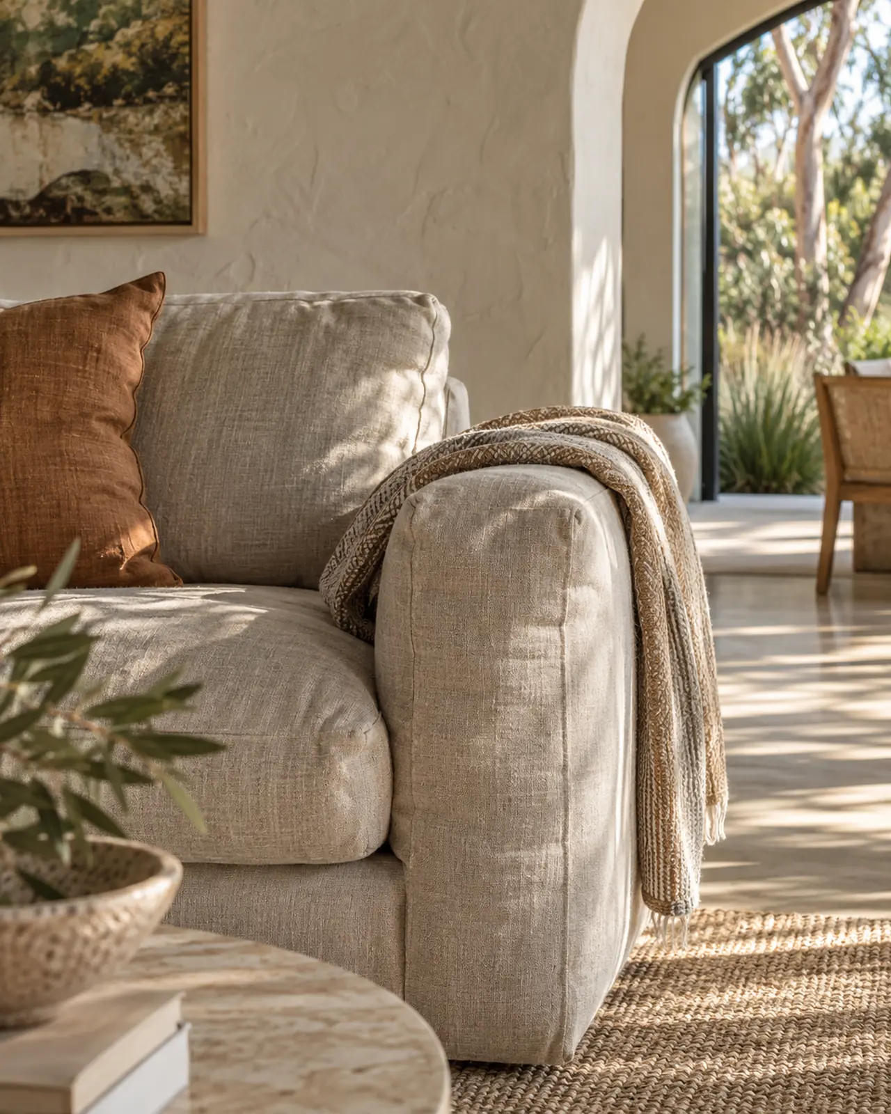 Creased oatmeal linen sofa arm with a folded throw beside a white rendered wall